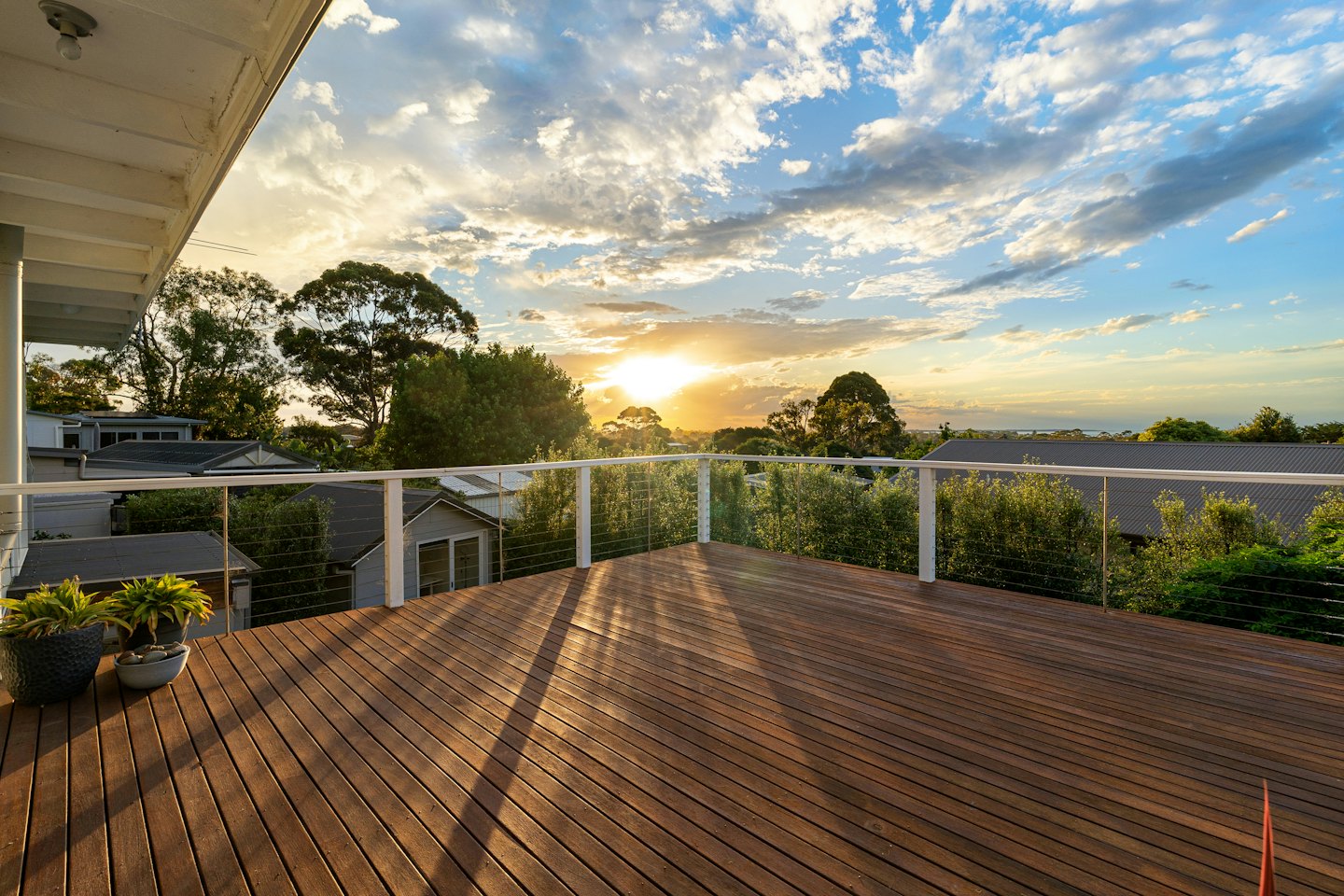 Wooden deck with cable railings overlooking suburban homes and trees.